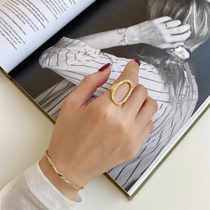 Detailed view of an irregular molten lava gold ring and wave bracelet on a hand