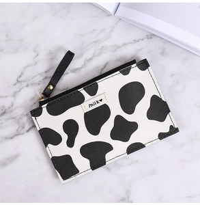 Close-up of cow print coin purse with zipper on marble surface and milk heart logo