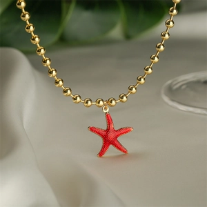 Detailed close-up of golden beaded necklace with vibrant red enamel starfish pendant
