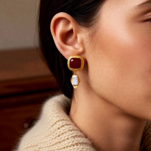 Close-up of vintage square red stone earrings with white charms on a model