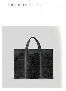 Detailed front view of black woven straw tote bag with decorative fringe and dual handles