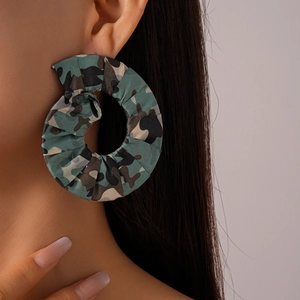 Gros plan de grandes créoles en tissu camouflage avec des motifs vert et marron texturés