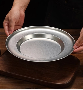 Close-up of a brushed stainless steel deep plate held by hands in a kitchen setting