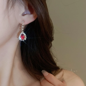 Close-up of elegant gold tassel earrings with red teardrop gems and sparkling rhinestones