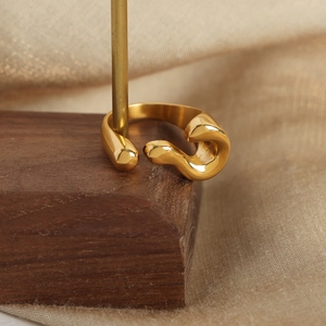 Abstract S-shape gold open ring on wooden stand with elegant silk fabric background