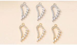 Macro detail of zircon-encrusted metal wing pendants in gold and silver finish