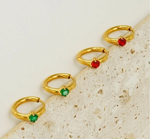 Detailed shot of gold plated earrings with red and green zircon stones on stone surface