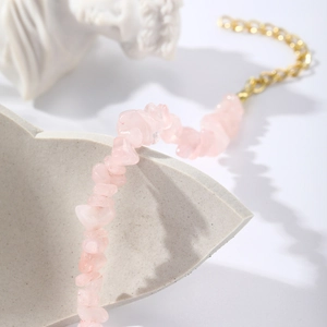 Macro detail of irregular pink crystal stones with gold chain on a minimalist tray