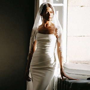 Detail of white satin bridal gown with floral lace veil under elegant natural window lighting