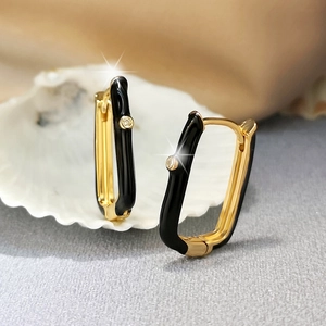 Macro shot of rectangular gold earrings with black enamel and a sparkling zircon inlay