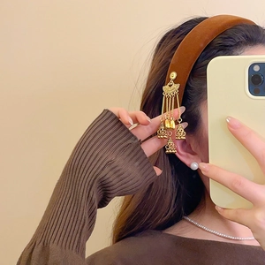 Close-up of model wearing brown velvet headband with golden tassels and pearl earrings