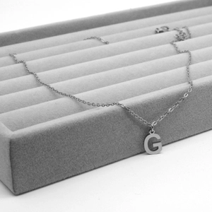 Close-up of a silver stainless steel G-letter pendant on a grey velvet display tray