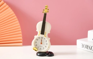 Dettaglio di una sveglia a forma di violino bianco su sfondo di scrivania rosa e bianca
