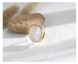 Detail of a minimalist gold ring with a round white shell inlay on a natural background