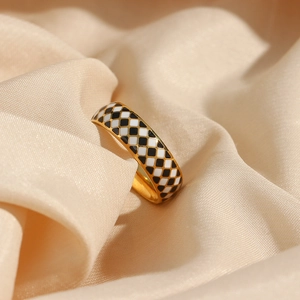 Close-up of gold ring with black and white checkered enamel on beige silk fabric