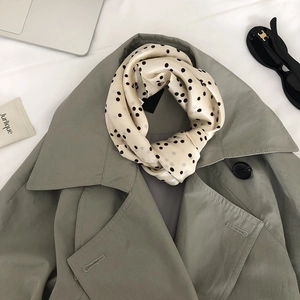 Detail of silk scarf with black polka dots styled with a trench coat on white fabric