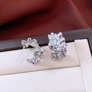 Macro detail of silver C-shaped earrings with pleats, white pearls, and sparkling crystals