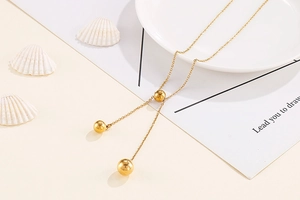 Close-up of golden stainless steel Y-necklace with adjustable ball pendants and shells