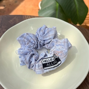 Close-up of light blue checkered scrunchie with pink heart clip and textile label