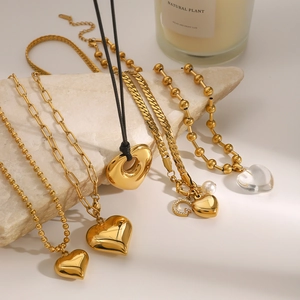Detailed shot of golden heart pendants and pearl necklace on a beige stone surface