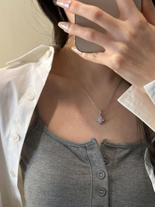 Close-up of a silver clover necklace with purple zircon stone worn by a model