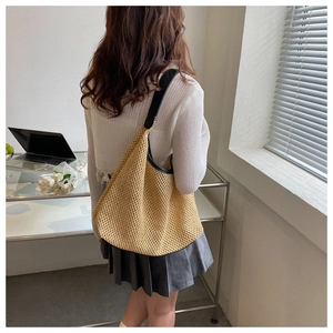Detailed woven texture of light brown straw tote bag with black strap on model