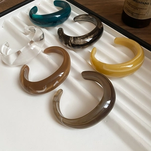 Close-up of vibrant acrylic open bracelets in six colors on a striped jewelry tray