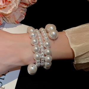 Detailed macro view of layered white pearl wrap bracelet on model's wrist with golden cuffs