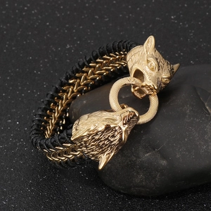 Macro detail of golden double wolf heads on a black braided leather bracelet for men