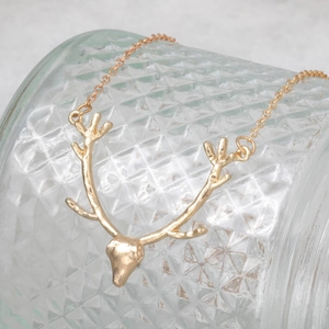 Golden reindeer antler pendant necklace displayed on a textured glass surface
