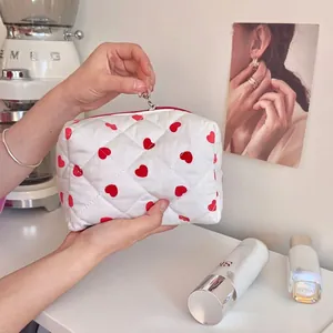 Quilted white cosmetic bag with red heart pattern on a minimalist dressing table