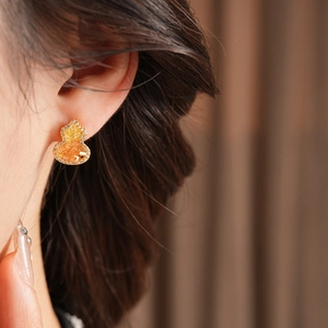 Gros plan détaillé d'un modèle portant une boucle d'oreille gourde dorée avec pierres oranges