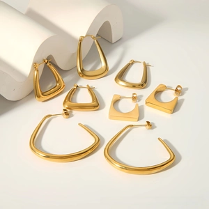 Close-up of golden geometric earrings including trapezoid and triangular shapes on white stone