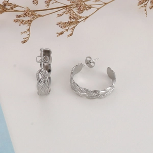 Detailed view of silver braided hoop earrings with metallic texture on beige surface