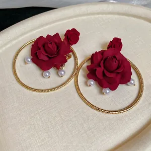 Elegant red fabric rose earrings with golden hoops and white pearl pendants on beige background