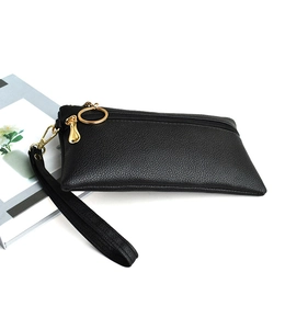 Detail of black lychee leather clutch bag featuring golden zipper and round ring puller