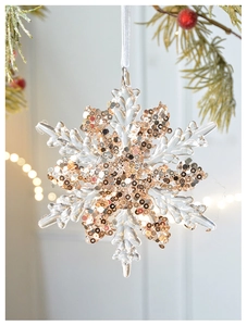 Close-up of snowflake Christmas ornament with gold sequins hanging on a pine branch