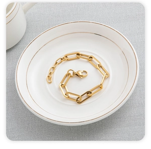 Detailed shot of golden paperclip chain bracelet in white ceramic dish with gold rim