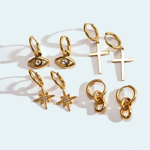 Detail of gold hoop earrings with star, cross, and evil eye charms in micro-pave crystals