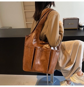 Brown PU leather tote bag with dual front pockets worn by model in a minimalist cafe setting