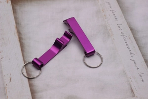 Close-up of purple aluminum bottle opener keychains on a soft beige fabric background