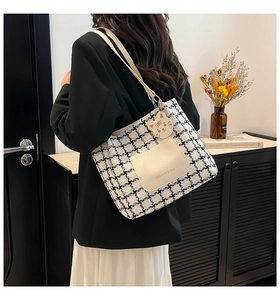 Detail of checkered tweed tote bag with leather pocket and cat pendant on a model