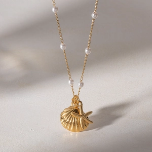 French ocean pearl necklace with gold starfish and shell pendants on textured background