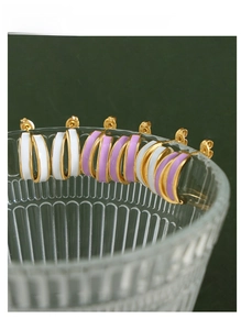 Close-up of gold-plated C-shaped earrings with white and lilac enamel on a glass rim