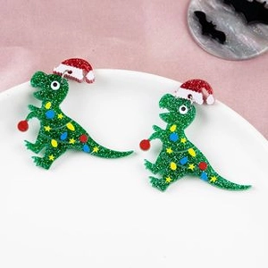 Close-up of green Christmas dinosaur earrings with red hats and glitter details