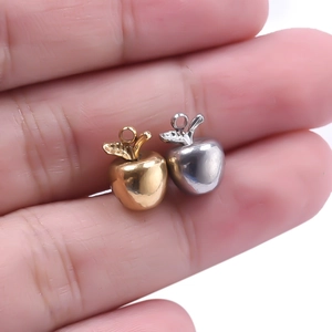 Macro shot of small gold and silver apple charms held on fingertips for size scale