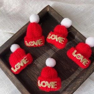 Close-up of five red mini knitted hats with LOVE gold glitter letters and white pom-poms
