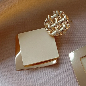 Detail of gold geometric earrings with woven texture and square sequins on silk fabric