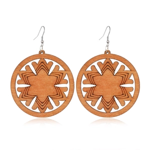 Detailed view of hollow wooden earrings with star pattern and metal hooks on white background