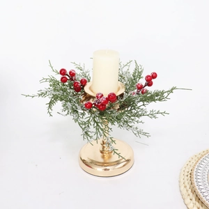 Close-up of golden candle holder with white candle, pine needles and snowy red berries
